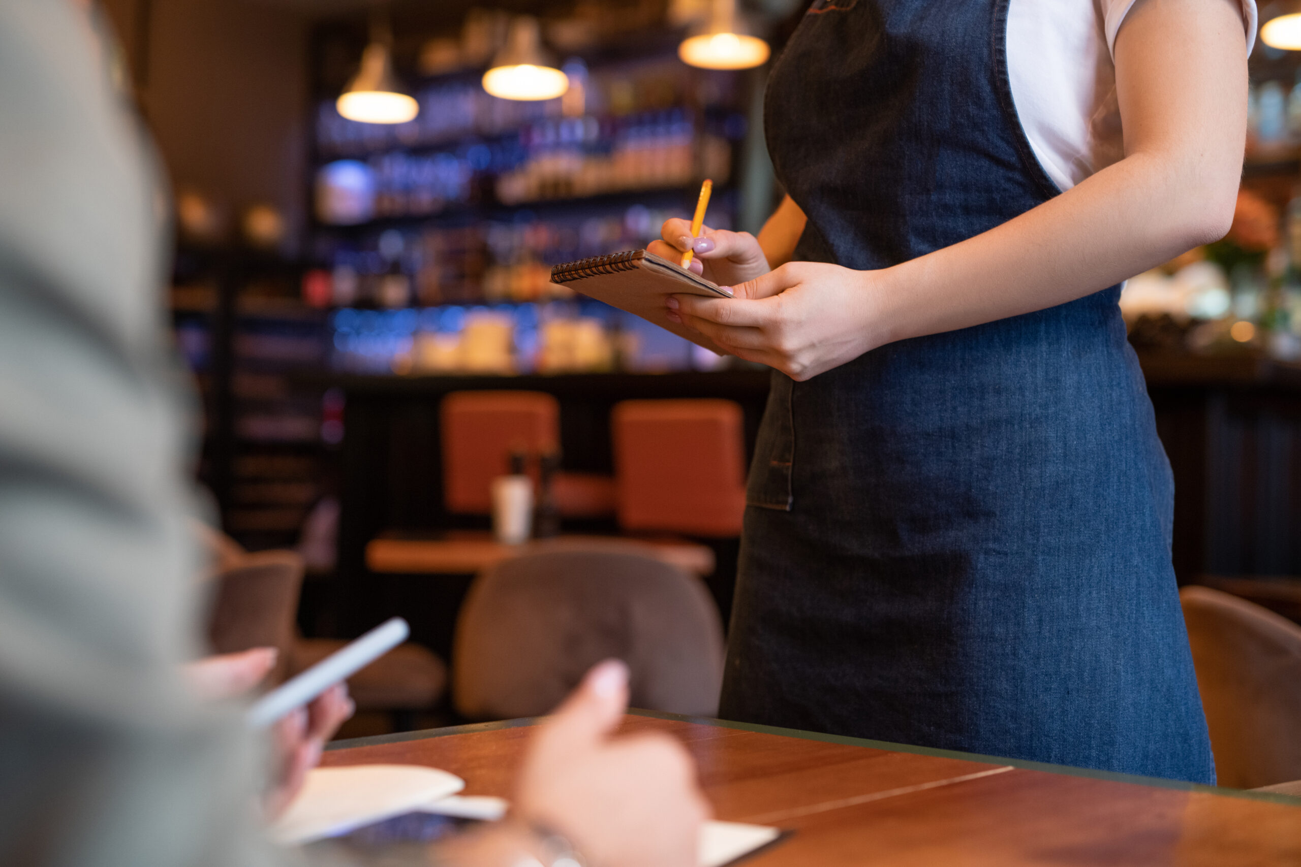 Hands of young waitress in apron wriitng down order of client in notepad